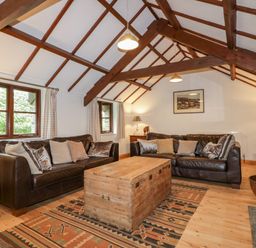 A living room with two leather sofas a wooden chest coffee table exposed wooden beams and patterned rugs at Ribby Barn in Lerryn