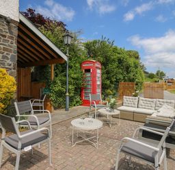 An outdoor seating area with chairs tables and a sofa near a red telephone booth at Llety Ceiro in Bow Street Wales