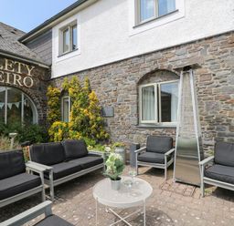 An outdoor seating area with black cushioned chairs and a metal patio heater in front of a stone building at Llety Ceiro Bow Street Wales