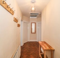 A hallway with wooden coat hooks on the wall a wooden table a ceiling light a wall mirror and parquet flooring at Ty Garth in Benllech