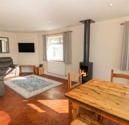 A living room with a gray sofa a wall-mounted TV a wood-burning stove a wooden dining table and chairs at Ty Garth in Benllech