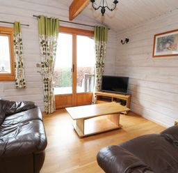 A living room with two brown leather sofas a wooden coffee table a small TV on a wooden stand floral curtains on windows at Barn Owl Lodge Rhayader