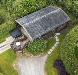 An aerial view of a small wooden cabin with a deck and outdoor furniture surrounded by greenery and paths at Barn Owl Lodge in Rhayader