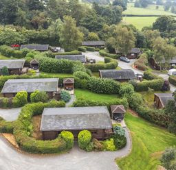 An aerial view of multiple wooden lodges with surrounding greenery and gravel paths at Barn Owl Lodge in Rhayader