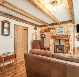 A living room with wooden beams, a leather sofa, an armchair, a fireplace, a wall clock, a small table, and a mounted TV at 48 High Street in Bridlington
