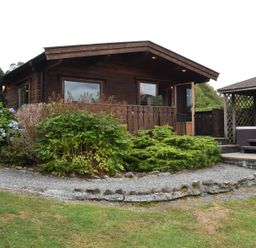 A wooden cabin with a gravel path garden shrubs and a hot tub gazebo at Hillside View in Rhayader