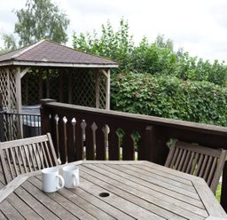 A wooden deck with a table and chairs and a gazebo with hot tub behind at Hillside View in Rhayader
