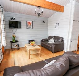 A living room with two brown leather sofas a wooden coffee table and a wall-mounted TV at Snowy Owl Lodge in Rhayader
