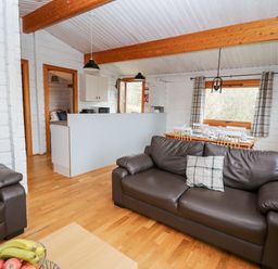 A living room with brown leather sofas a dining table set with dishes and cutlery and a kitchen area at Snowy Owl Lodge in Rhayader