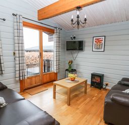 A living room with two leather sofas a wooden coffee table a wall-mounted TV and sliding glass doors at Snowy Owl Lodge in Rhayader