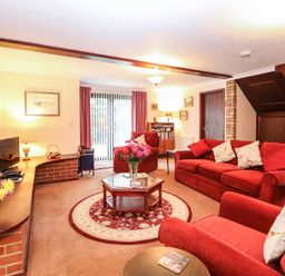 A living room with red sofas a round rug and a glass top coffee table at Walnut Tree Cottage in Catfield
