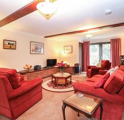 A living room with red sofas a wooden coffee table a television and paintings on walls at Walnut Tree Cottage in Catfield