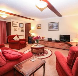 A living room with red sofas armchairs a coffee table and a television at Walnut Tree Cottage in Catfield