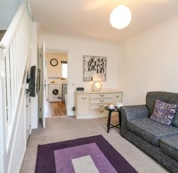 A living room with a gray sofa with purple pillows a purple rug a white staircase and a sideboard at Kingfisher Cottage in Weymouth