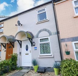 Exterior view of a row of terraced houses with small garden plants and covered porches at Kingfisher Cottage in Weymouth