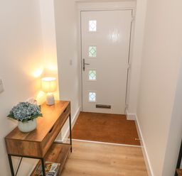 An entryway with a wooden table holding a lamp and flowers next to a white door at Berth in Afonwen near Criccieth