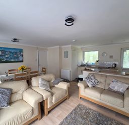 An open living room and kitchen area with cream sofas and wooden dining table at 17 River Banks in Liskeard