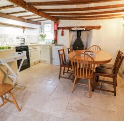 A kitchen and dining area with wooden chairs around a table and a wood stove at Teign Cottage in Shaldon