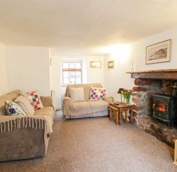A living room with two sofas a stone fireplace with a wood stove and wooden side tables at Teign Cottage in Shaldon