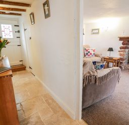 A hallway with a wooden console table and flowers next to a living room with sofas a side table and a fireplace at Teign Cottage in Shaldon