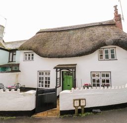 A white thatched cottage with a small black gated patio and pink flowers at Teign Cottage in Shaldon