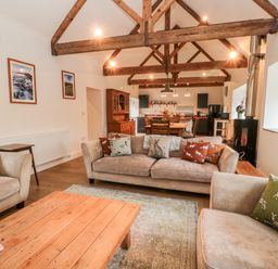 An open plan living room and kitchen with wooden beams on the ceiling and sofas with animal print cushions at The Old Workshop in Middleton near Belford