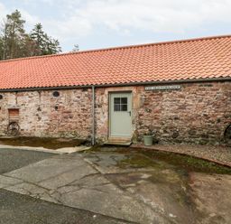 The exterior of a stone building with a red tiled roof a door a window and old wagon wheels at The Old Workshop in Middleton near Belford