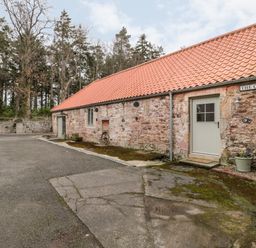 An exterior view of a stone building with a tiled roof and multiple doors with a paved area in front at The Old Workshop in Middleton near Belford