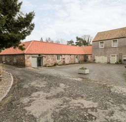 A courtyard with stone buildings and a gravel driveway at The Old Workshop in Middleton near Belford