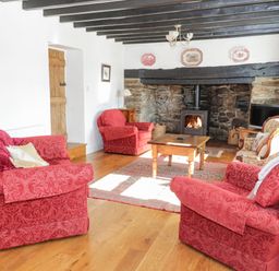 A living room with red armchairs a wooden coffee table a stone fireplace and a television at Tyn Llwyn in Pencoed near Corwen