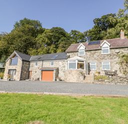 A stone house with a gravel driveway a patio area and green trees behind at Tyn Llwyn in Pencoed near Corwen