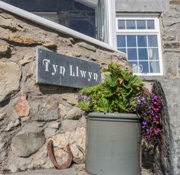 A stone wall with a sign reading Tyn Llwyn a potted plant and a horseshoe at Tyn Llwyn in Pencoed near Corwen