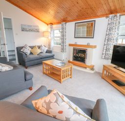 A living room with sofas, a coffee table, a fireplace, a television on a stand, and windows with curtains at Smugglers Shack in Polperro