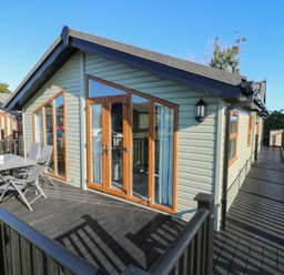 An outdoor deck with table and chairs attached to a single story cabin with large windows and wooden doors at Smugglers Shack in Polperro