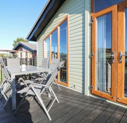 An outside deck with a metal table and six chairs attached to a building with large glass windows and wooden frames at Smugglers Shack in Polperro