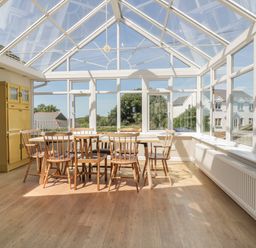 A conservatory with a table and wooden chairs and a yellow storage cabinet at Auverne in Poundstock near Widemouth Bay