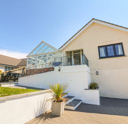 A white house with a glass conservatory and a small garden area at Auverne in Poundstock near Widemouth Bay