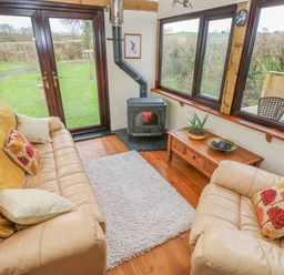 A living room with leather sofas a wood stove a coffee table and large windows showing a garden at Sarngwm in Narberth