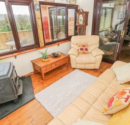 A sitting area with beige armchair and sofa a wooden coffee table a rug and a wood burner at Sarngwm in Narberth