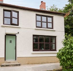 Exterior of a two story house with textured walls green door and brown framed windows with plants nearby at Fisherman's Cottage in Llandysul