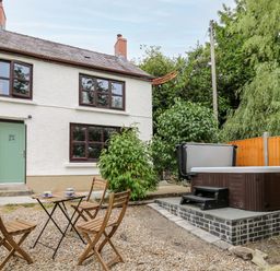 A backyard with wooden chairs and table with cups and a hot tub near a white house with green door and brown windows at Fisherman's Cottage in Llandysul