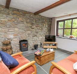 A living room with stone wall fireplace two armchairs wooden chest coffee table and window at Fisherman's Cottage in Llandysul