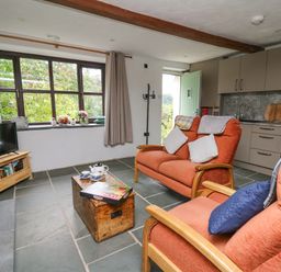 A living room with orange armchairs a wooden coffee table and a kitchenette at Fisherman's Cottage in Llandysul