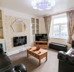 A living room with two black sofas a wooden coffee table a mounted television and a window with curtains at The Vale in Ashwater