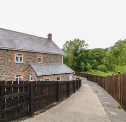 A stone house with white framed windows beside a paved driveway and wooden fences at The Vale in Ashwater