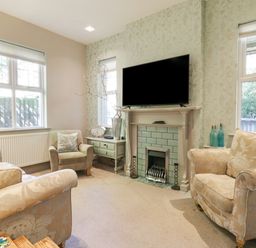 A living room with armchairs a fireplace a television on the mantel and windows at Saxon Lodge Cottage in Felixstowe Suffolk