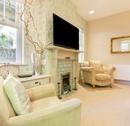 A sitting room with two armchairs a fireplace and a television mounted above at Saxon Lodge Cottage Felixstowe Suffolk
