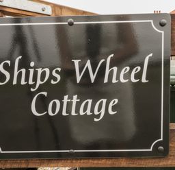A black and white sign reading Ships Wheel Cottage on a wooden fence at Shipswheel Cottage at Broadings Farm Whitby