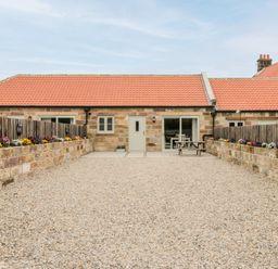 A stone house with a red tiled roof and a gravel courtyard with flowerbeds and a picnic table at Shipswheel Cottage at Broadings Farm in Whitby