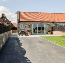 An exterior view of a stone building with a red tiled roof a paved area a wooden picnic table two flower pots a lawn and wooden fencing at Stag Cottage at Broadings Farm in Whitby